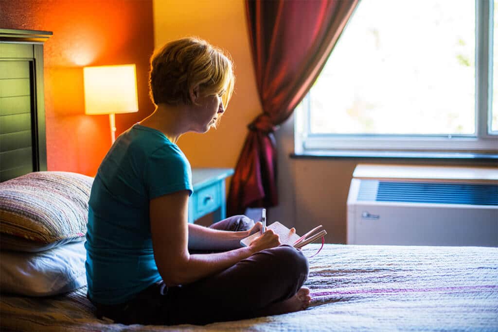 A young woman writes in her journal while sitting on her bed