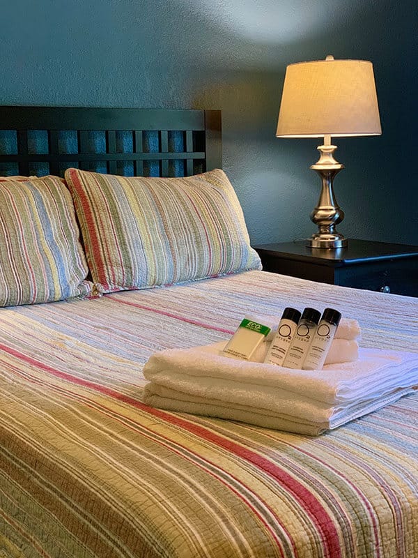 A made bed with a cozy bedspread has towels and toiletries sitting on top