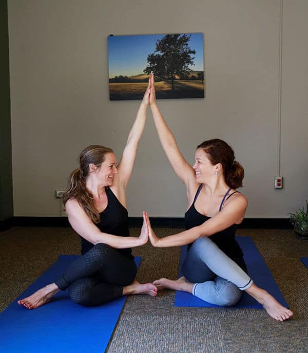 Two young women make a yoga pose together touching palms