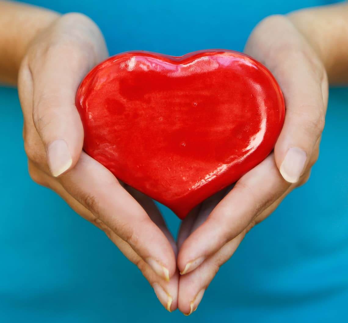 Two hands hold a red ceramic heart