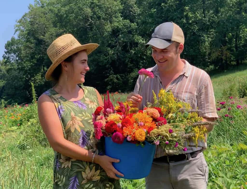 A smiling man and woman hold a huge bucket of bright summer flowers together