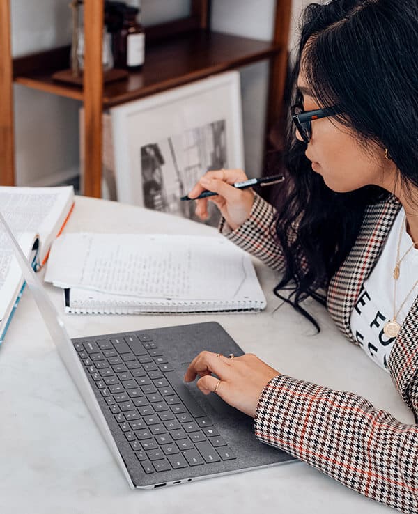 A young woman studies with her laptop open and writes in a notebook