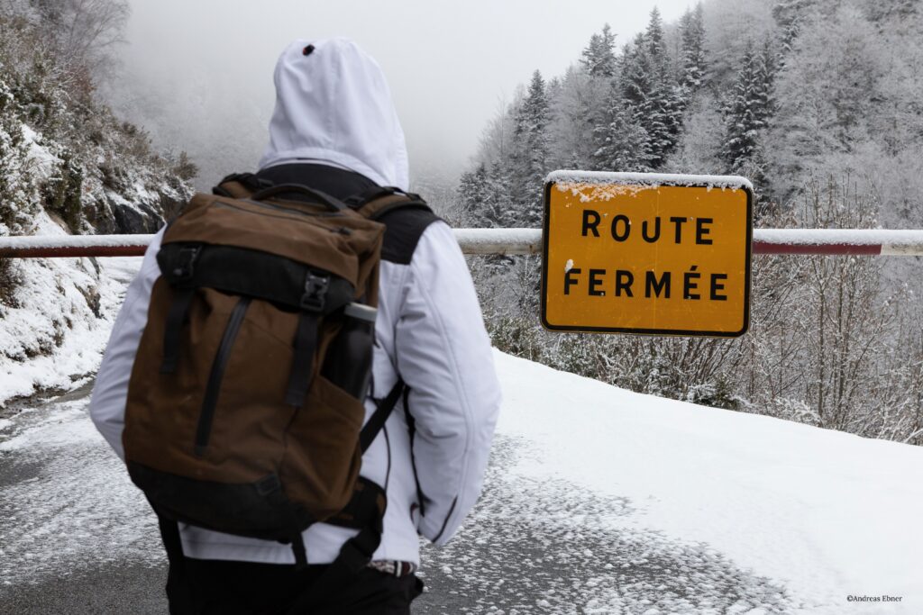 Snowy trailhead with gate and sign: A person contemplates the trail ahead.