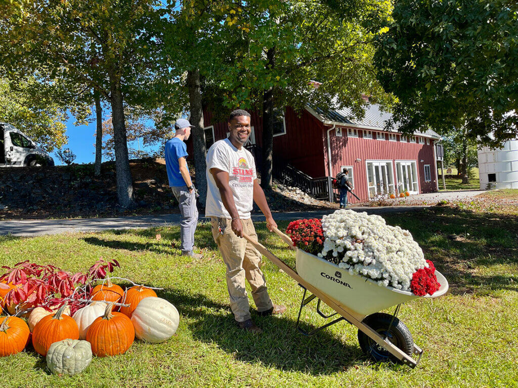 man smiling with wheelbarrow full of flowers