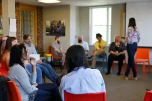 A seated group of people in a circle talking at a mental health day program