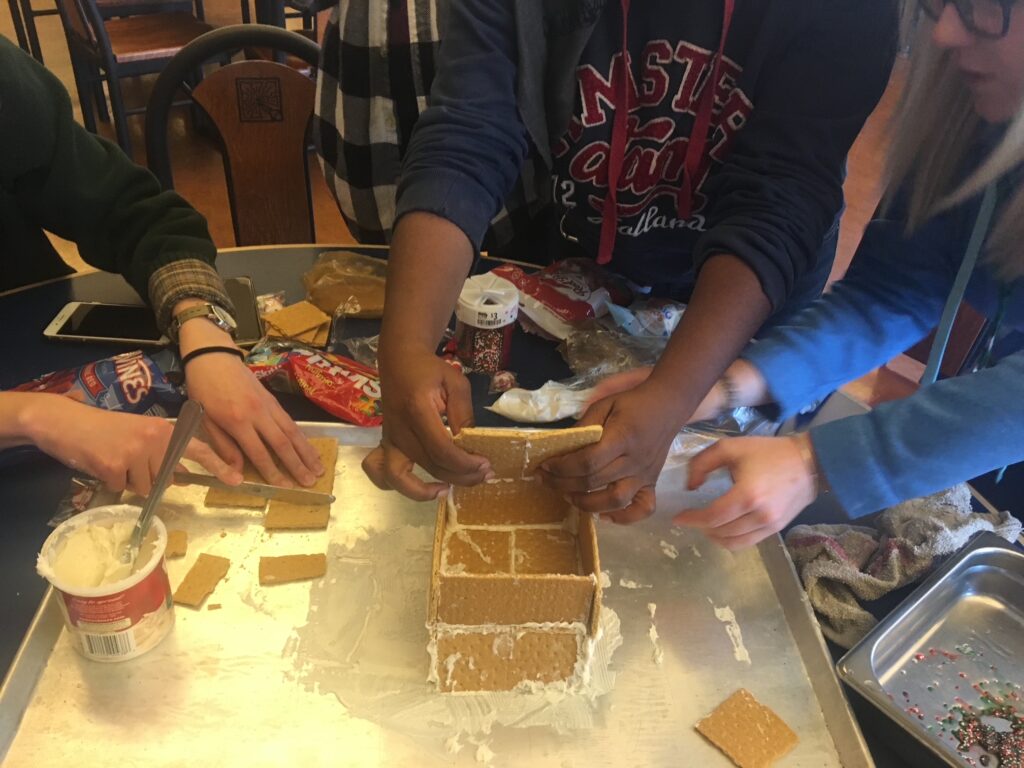 three people making holiday graham cracker house