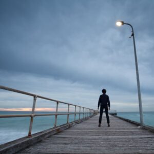 a man stands alone on a pier with a moody sky. can schizophrenia be cured?