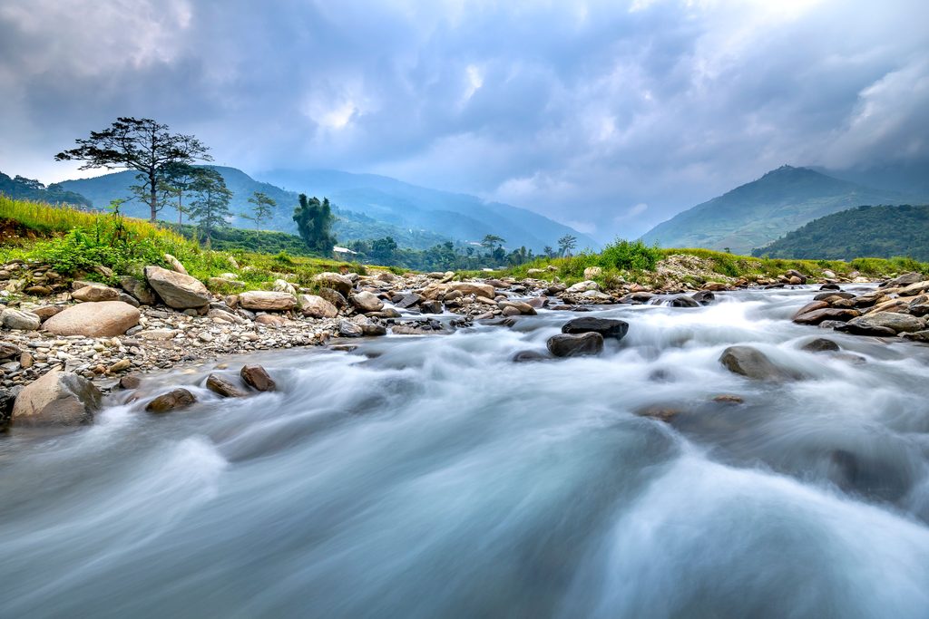 A river flows with green mountains and deep blue clouds in the background. Grounding techniques for anxiety that induce flow state.